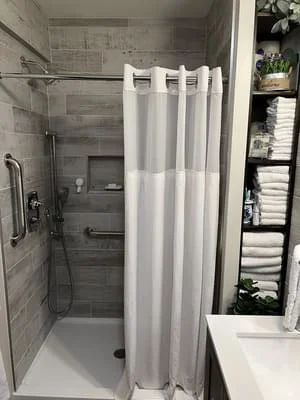 Walk-in shower with gray tile, glass enclosure, chrome fixtures, and white vanity