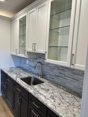 Two-tone kitchen with white and dark cabinets, granite countertops, blue tile backsplash, and stainless steel sink