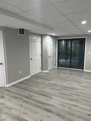 Finished basement with gray wood-look vinyl flooring, white trim doors, and recessed lighting
