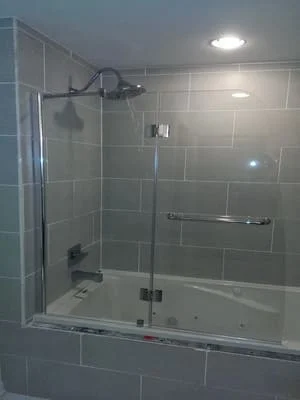Frameless glass shower enclosure with pivot door and brushed nickel hardware over subway tile