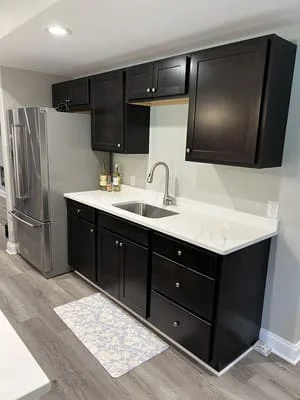 Black cabinetry kitchen with white quartz countertop, stainless steel sink, and gray vinyl flooring