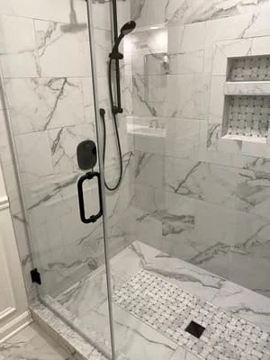 Frameless glass shower with marble tile walls, rainfall showerhead, and matte black fixtures