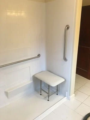 Walk-in shower with grab bars, transfer bench, and white subway tile walls