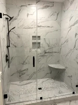 Marble tile shower with frameless glass door, built-in niche, and mosaic floor tile