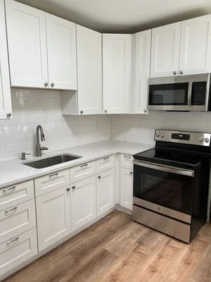 White shaker cabinets, subway tile backsplash, stainless steel range and microwave, wood flooring