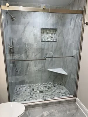 Gray marble tile shower with frameless glass door and mosaic tile floor
