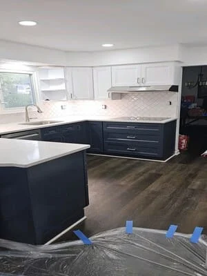 Two-tone kitchen with white upper and navy lower cabinets, white quartz counters, subway tile backsplash, and island