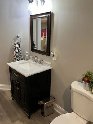 Black vanity cabinet with white marble countertop and framed mirror in bathroom