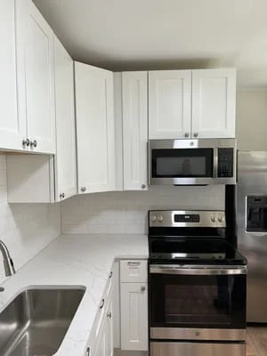 White kitchen cabinets with quartz counters, stainless steel appliances, and black wall ovens