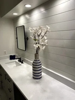 White quartz vanity with gray shiplap wall, recessed lighting, and framed mirror