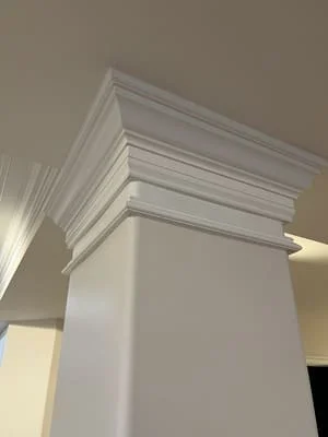 Layered crown molding and trim detail on white painted column with multi-profile design