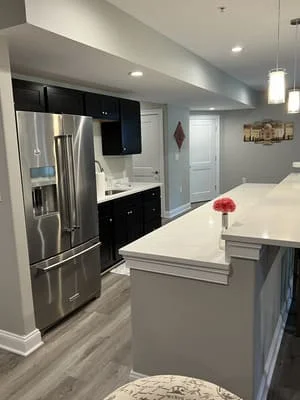 Modern kitchen with black cabinets, stainless steel appliances, white island, and gray flooring