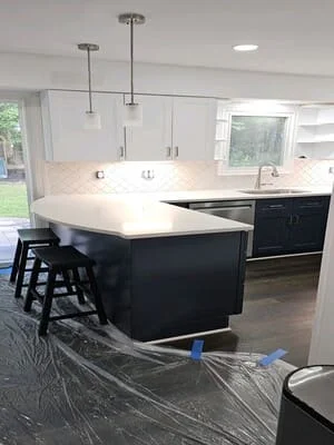 Black kitchen island with white quartz counters, pendant lights, white cabinetry, and stainless steel appliances