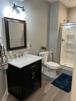Black vanity with marble top, framed mirror, and glass-enclosed shower in renovated bathroom