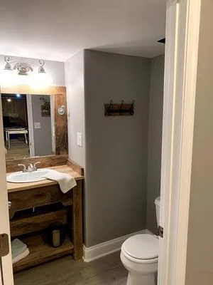 Bathroom with wooden vanity, gray tile walls, white toilet, and updated lighting fixtures